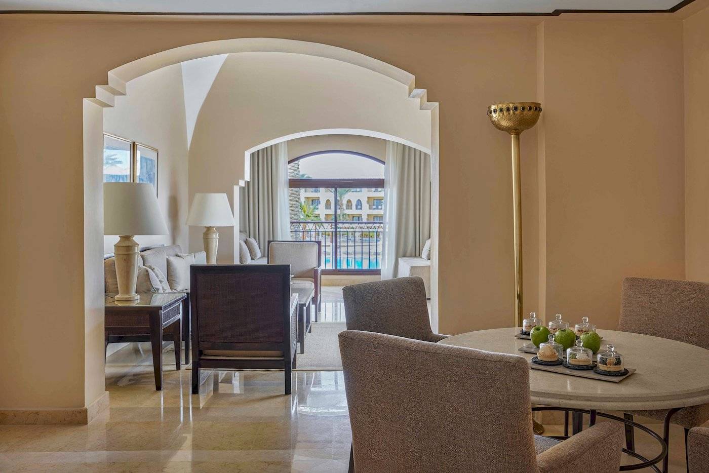 Innenansicht des Wohnbereichs im Jaz Lamaya Resort mit Tisch, Stühlen und Blick auf einen Swimmingpool.