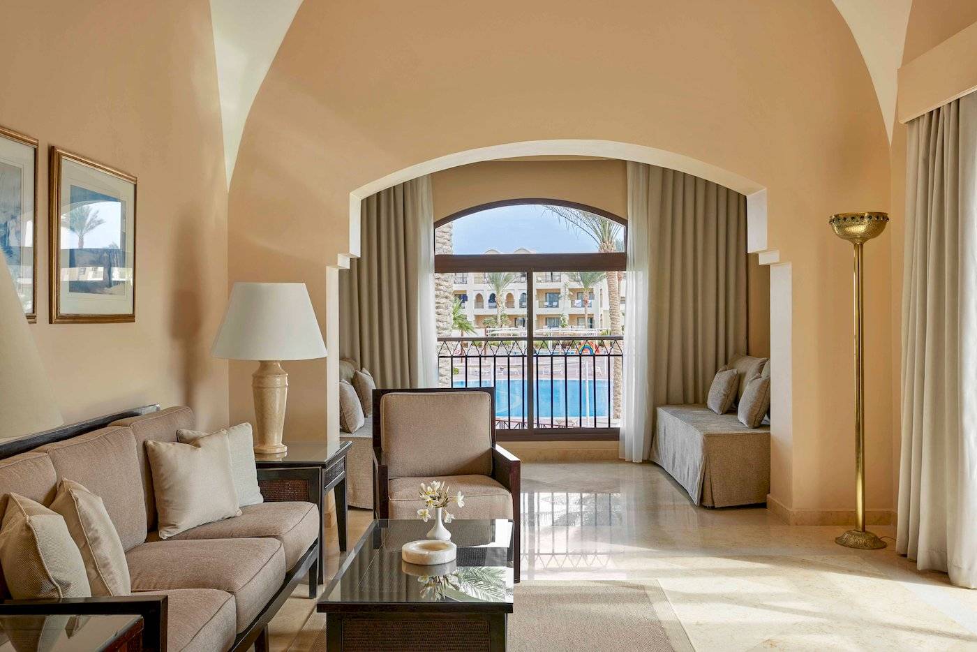 Wohnzimmer des Jaz Lamaya Resorts mit Sofa, Tisch, Lampe und Terrassenfenster mit Poolblick