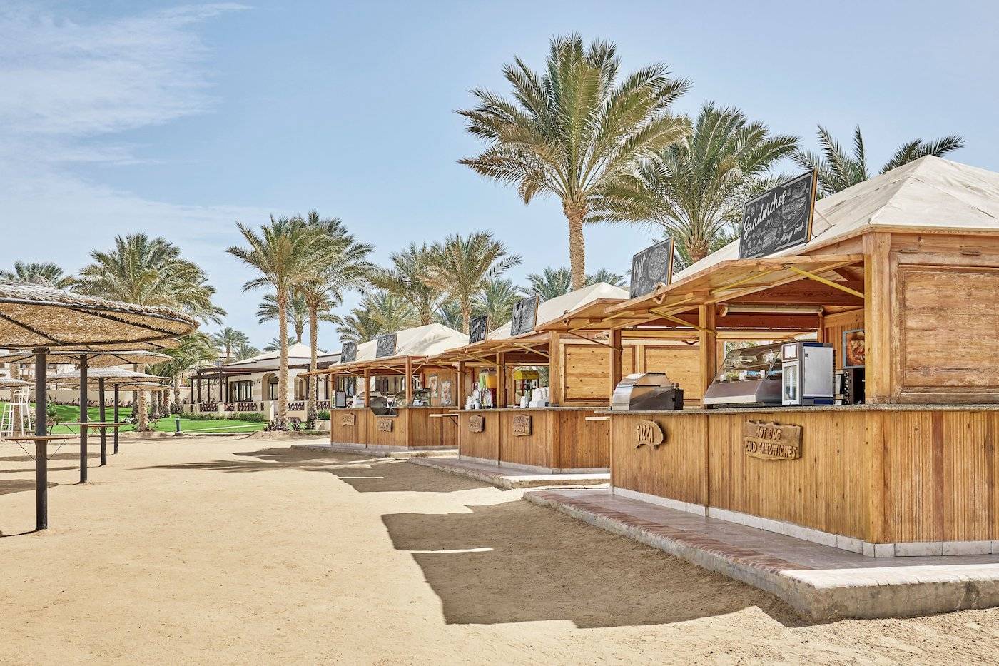 Strandimbissbuden im Jaz Lamaya Resort mit Holzhütten und Palmen im Hintergrund.