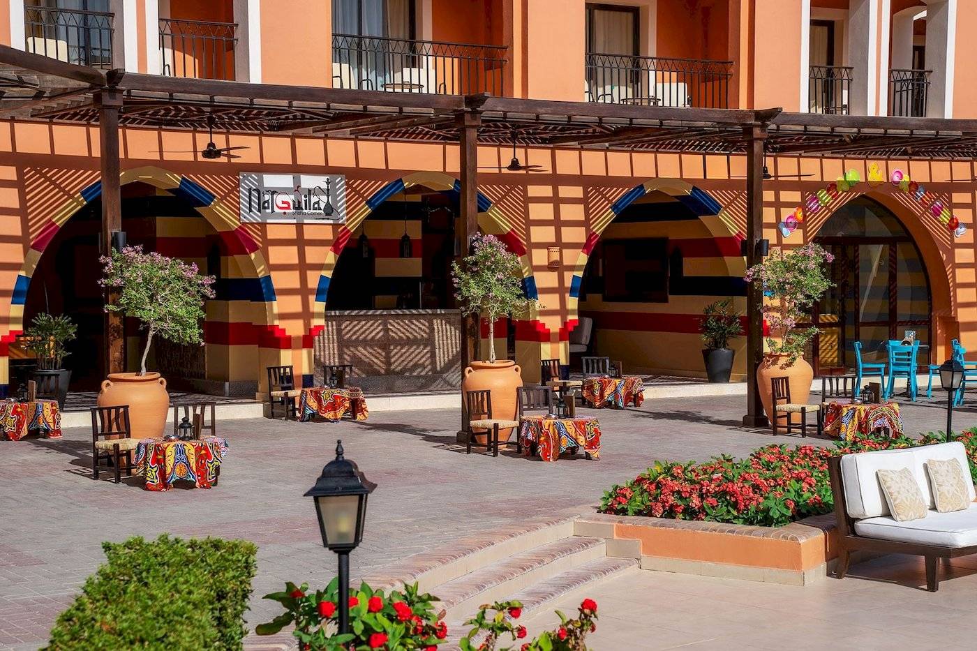 Lounge-Bereich des Jaz Lamaya Resorts mit bunten Tischen, Stühlen und Blumenbeeten.