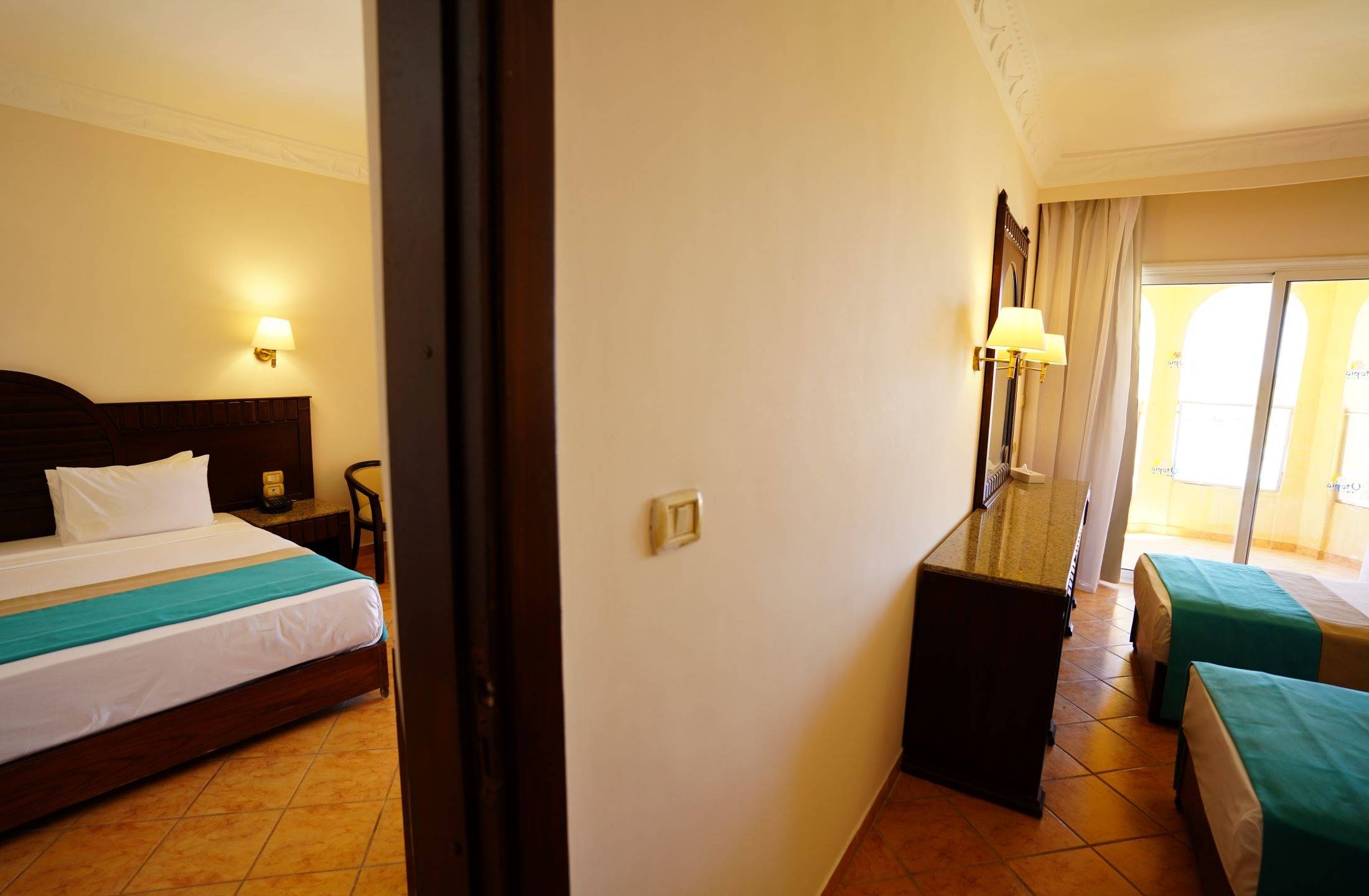 Innenansicht eines Hotelzimmers im Utopia Beach Club, mit einem Bett, einem Nachttisch und einer Terrasse.