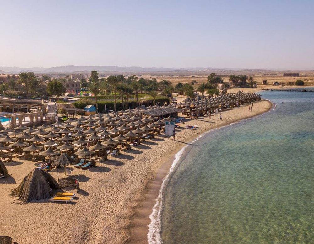 Luftaufnahme des Utopia Beach Club Strands mit vielen Sonnenschirmen und Hotelgebäuden