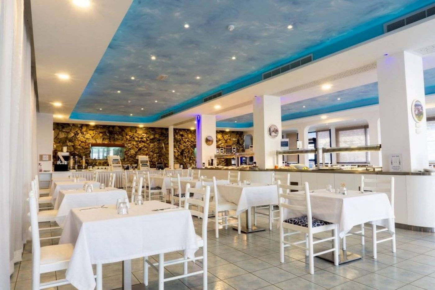 Innenbereich des Anonymous Beach Hotels mit blauem Himmel-Decke, weißen Tischen und Stühlen.