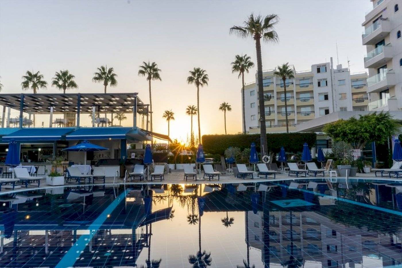 Der Swimmingpool des Anonymous Beach Hotels bei Sonnenuntergang mit Lounge-Stühlen und Palmen.