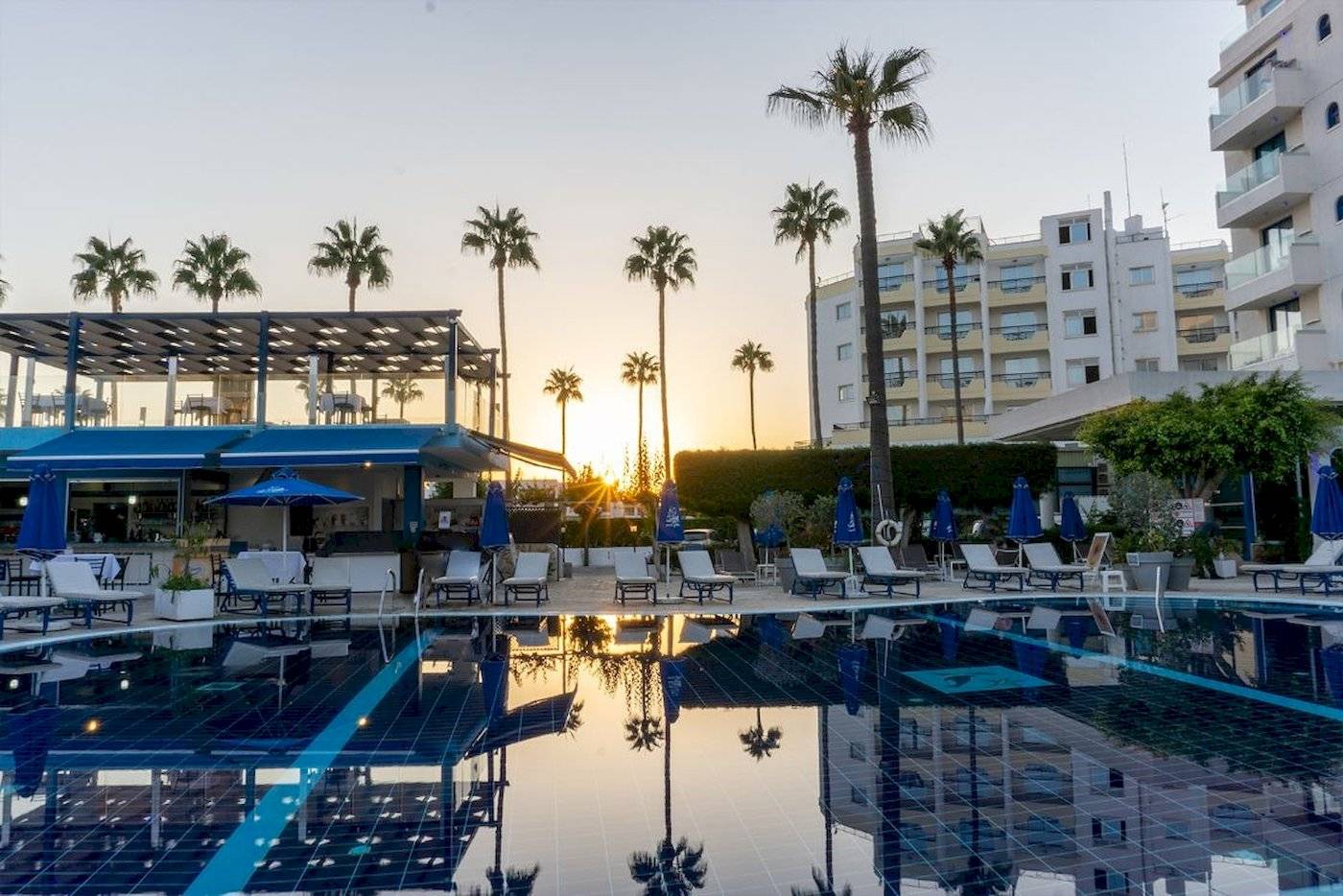Sonnenuntergang am Swimmingpool des Anonymous Beach Hotels mit Lounge-Stühlen und Palmen.