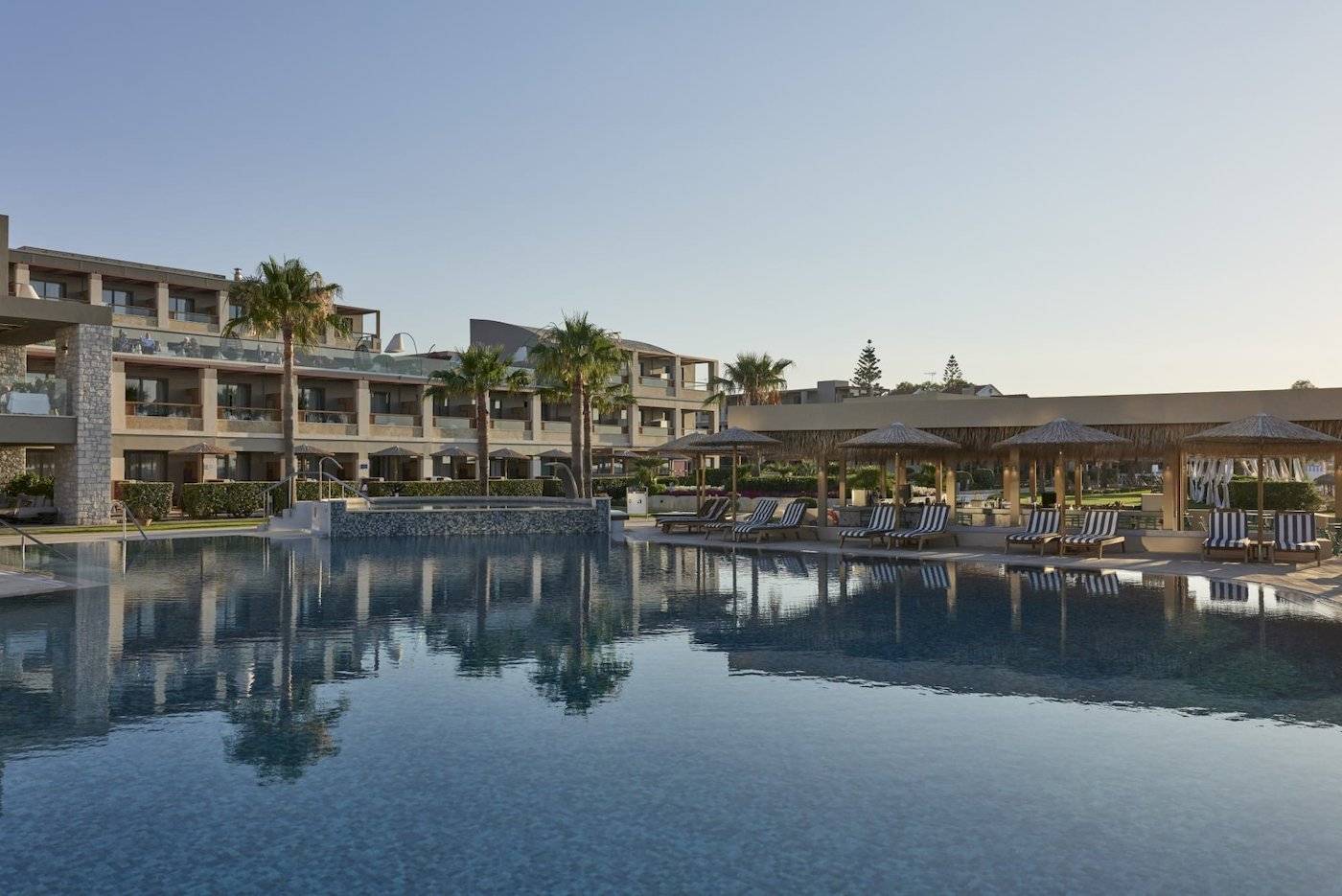 Außenpoolbereich des Atlantica Kalliston Resorts mit Lounge-Liegestühlen und Sonnenschirmen.