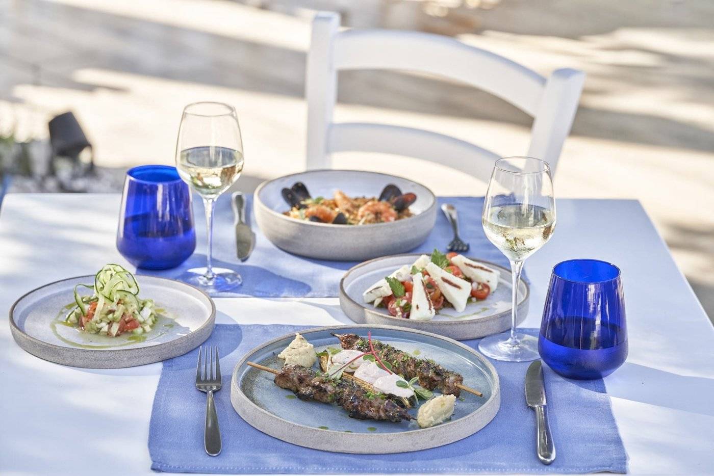 Mehrere Gerichte und Gläser Wein auf einem Tisch im Freien im Atlantica Kalliston Resort.