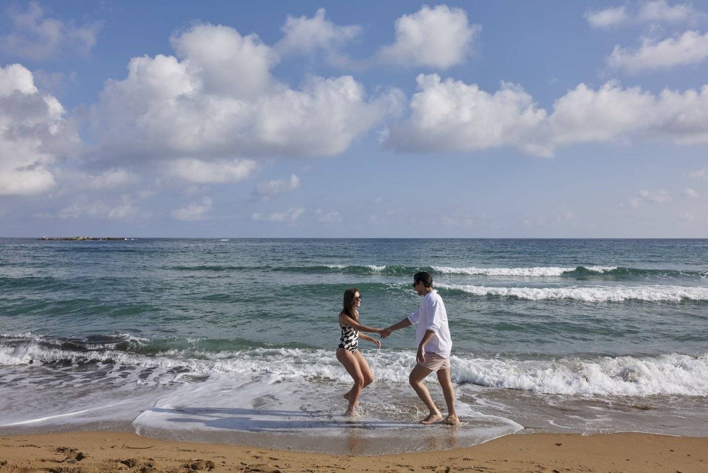 Paar im Wasser am Strand vor blauem Himmel mit Wellen und weißen Wolken