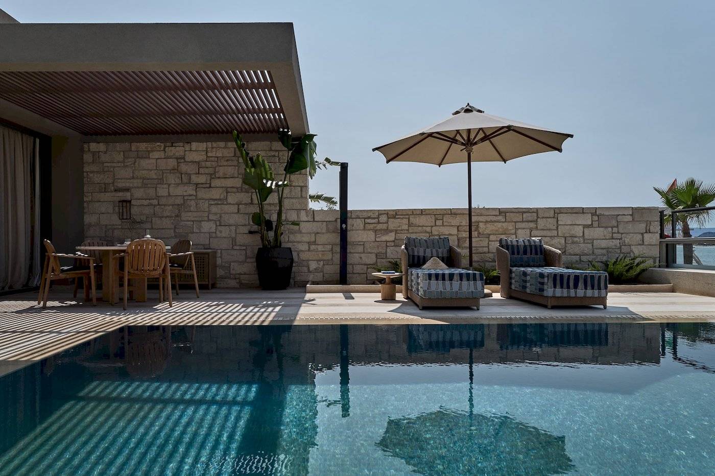 Terrasse des Atlantica Kalliston Resorts mit Sonnenschirm und Sesseln neben einem Pool.