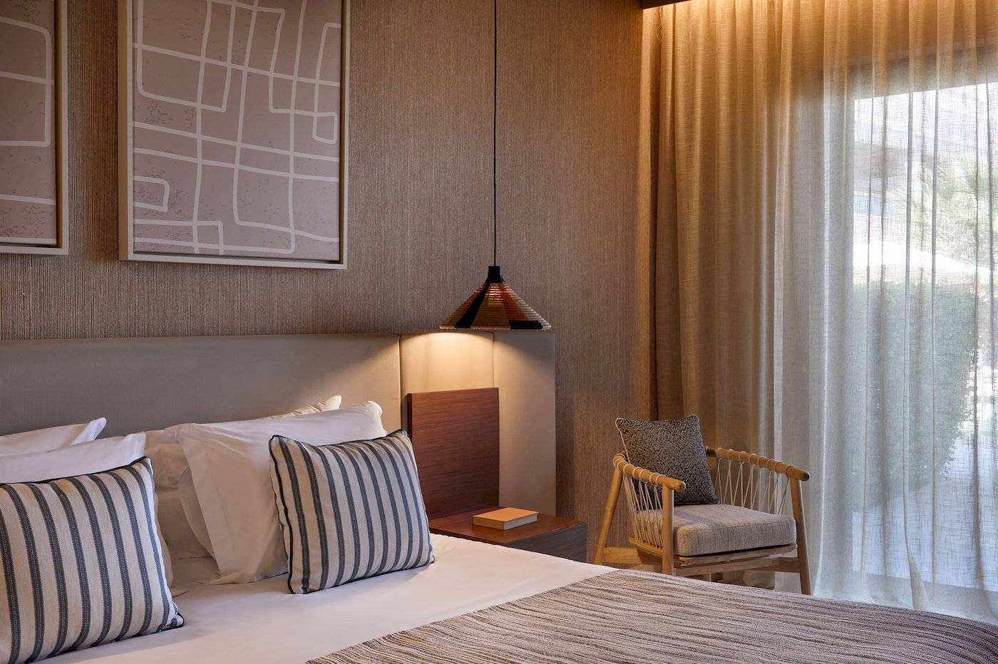 Ein elegantes Hotelzimmer mit Doppelbett, Kissen, Nachttisch und hängender Lampe im Atlantica Kalliston Resort.