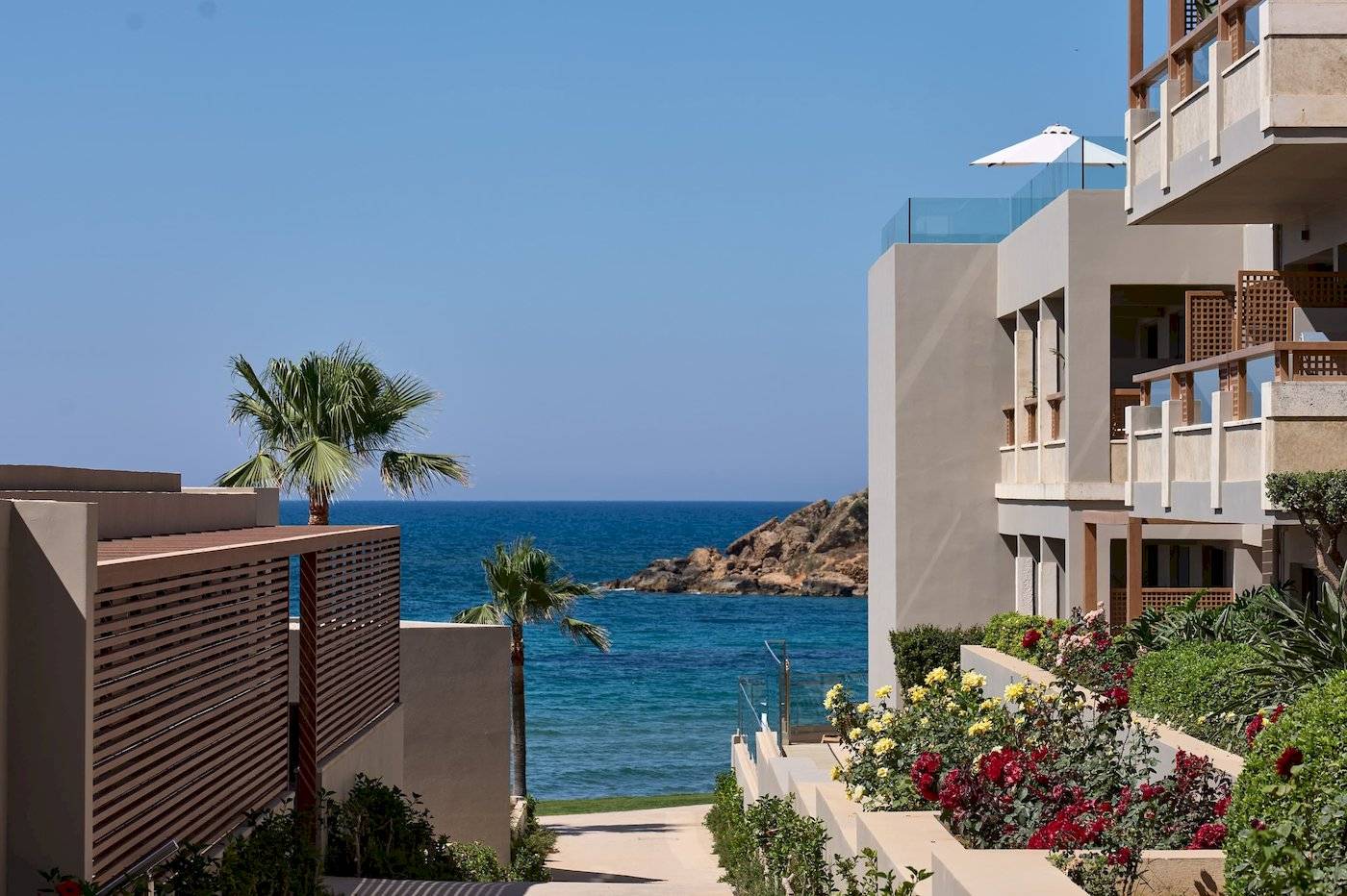 Außenansicht des Atlantica Kalliston Resorts mit Blick auf das Meer und eine Terrasse mit Sonnenschirm.