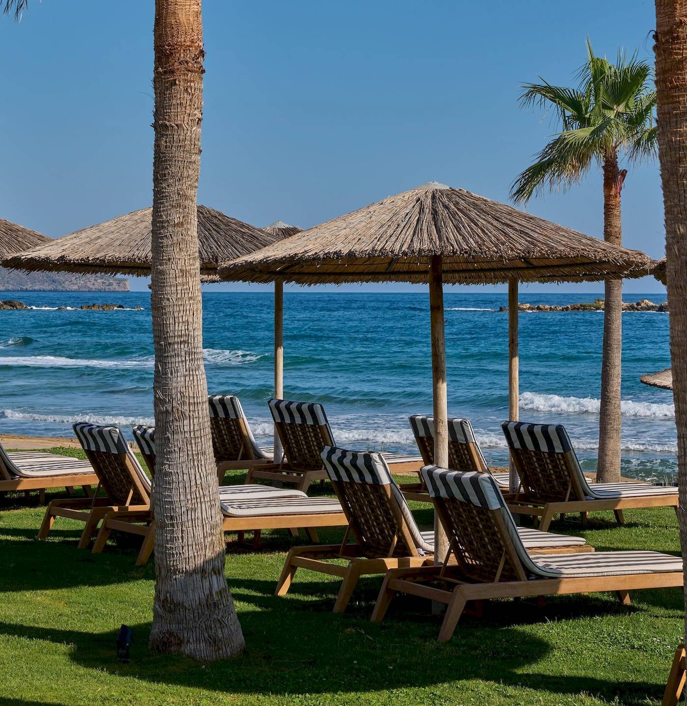 Strand-Lounge-Stuhle unter Palmenbaumen am Atlantica Kalliston Resort.