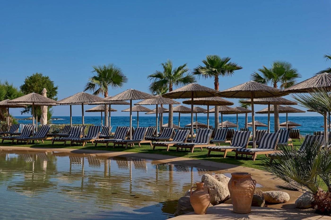 Atlantica Kalliston Resort Strand mit Lounge-Stühlen und Sonnenschirmen