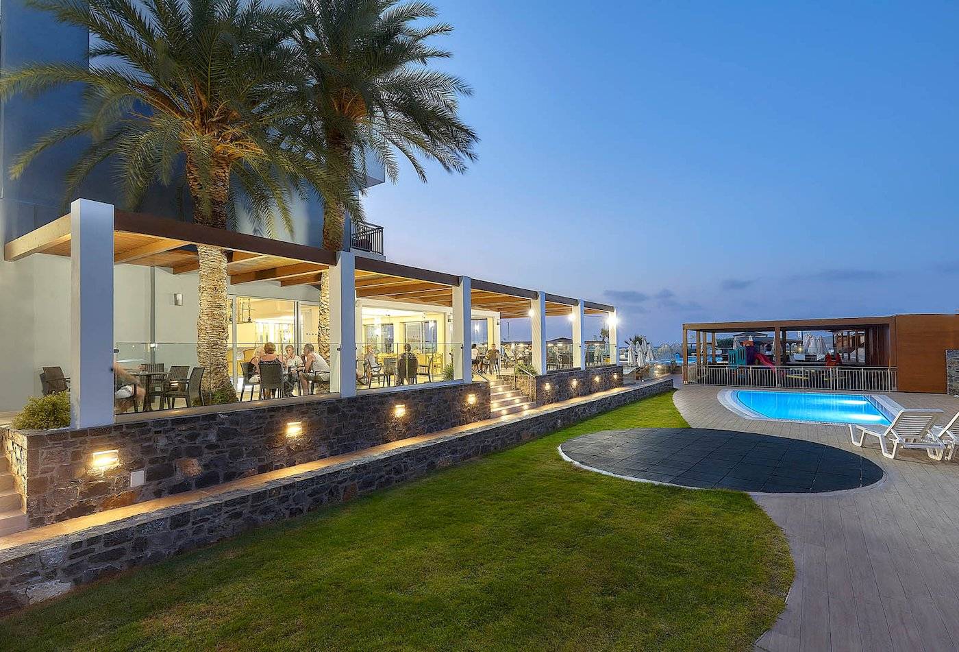 Terrasse des Astir Beach Hotels auf Kreta bei Abendbeleuchtung mit Palmen und Pool.