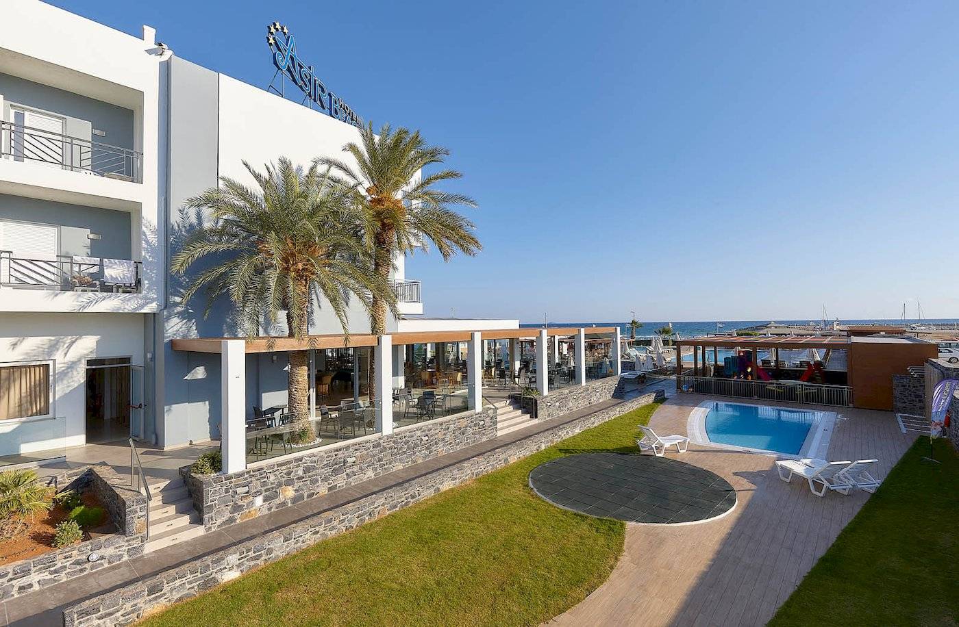 Außenansicht des Astir Beach Hotels auf Kreta mit Swimmingpool, Palmen und Terrasse.