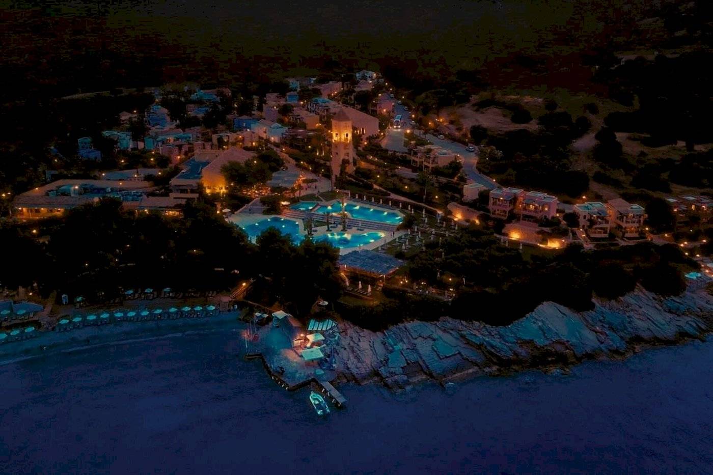 Nachtansicht des Candia Park Village Hotels mit beleuchteten Gebäuden und Pools