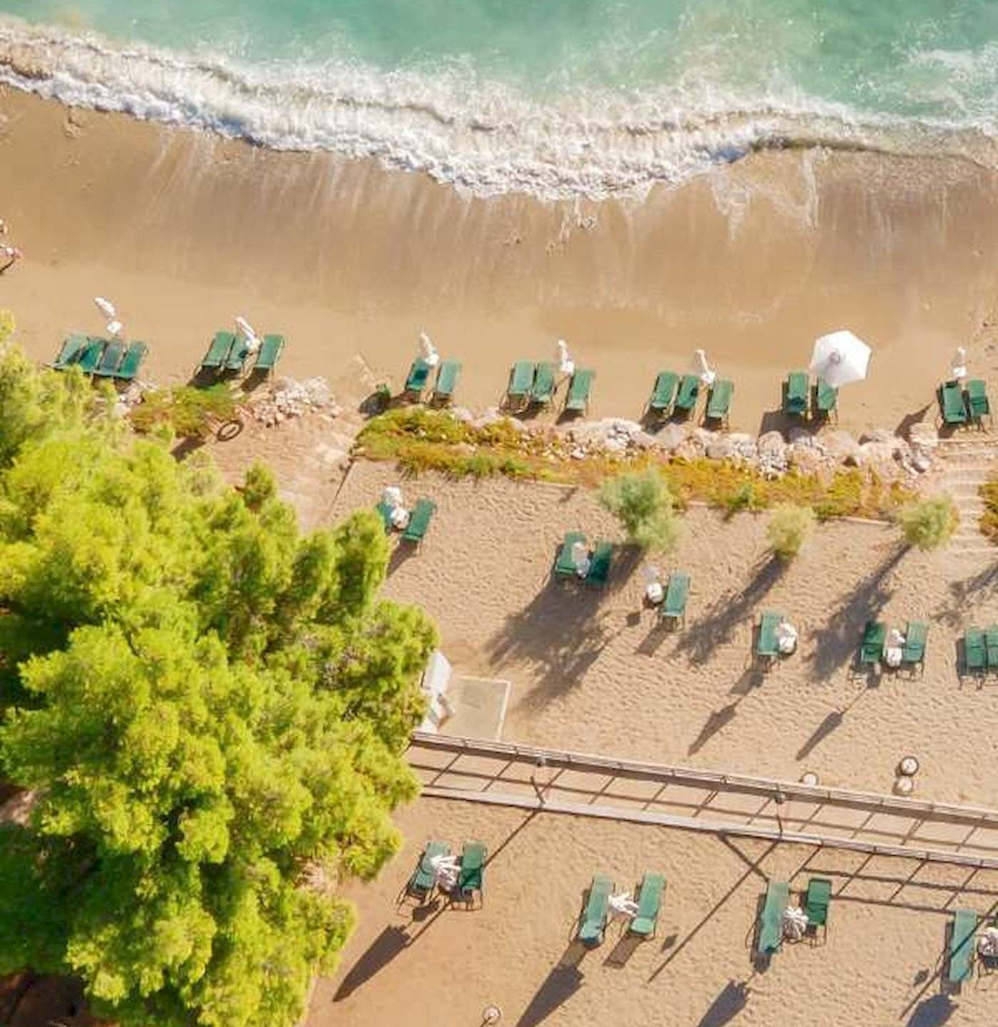 Luftaufnahme des Candia Park Village Strandes mit grünen Liegen und weißen Sonnenschirmen.