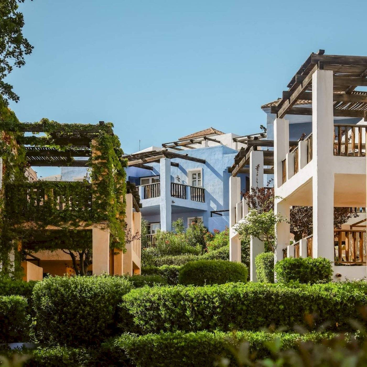 Außenbereich des Candia Park Village Hotels mit blauen und weißen Gebäuden und grünen Büschen