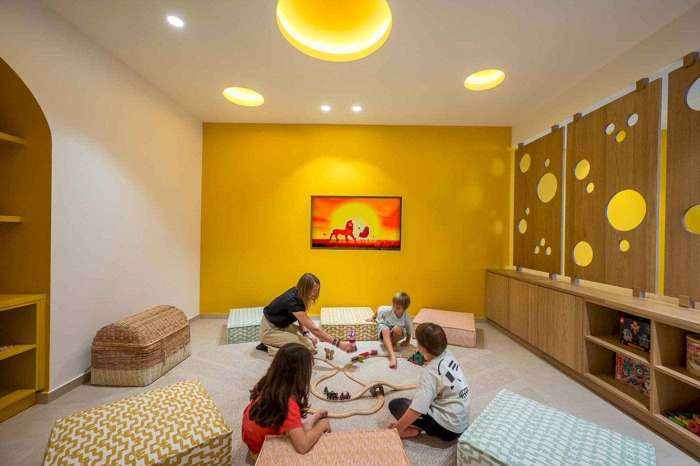 Arminda Hotel Kinderspielzimmer mit gelben Wänden, Holzmöbeln und Spielen.