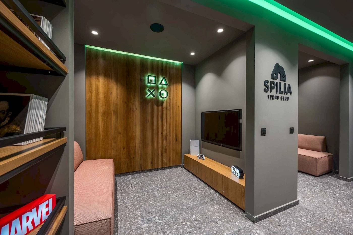 Innenbereich des Spilia Teens Club mit einer Couch, einem Fernseher und einem Regal mit Büchern.