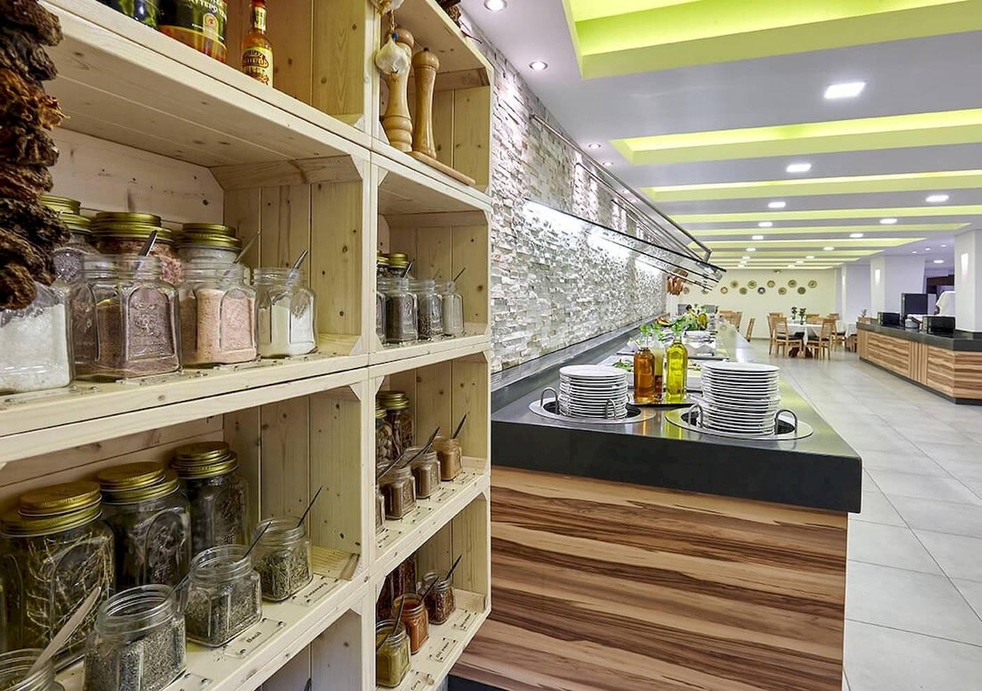 Innenbereich des Arminda Hotel & Spa mit Regalen voller Gewürzgläser und einer Theke mit gestapelten Tellern.