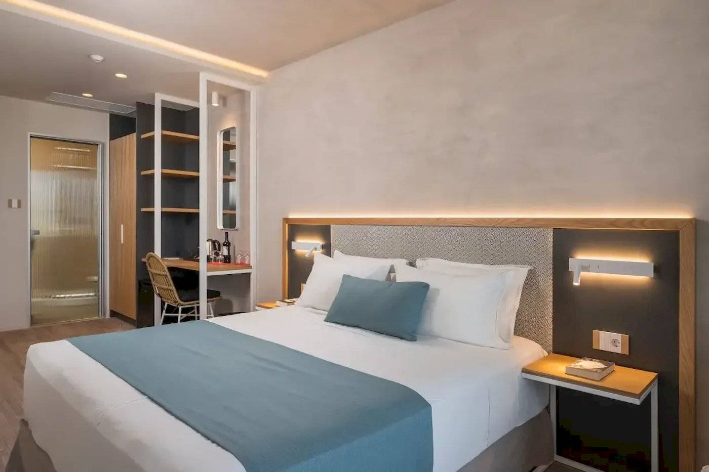 Inneneinrichtung eines Zimmers im Corissia Beach Hotel mit Bett, Schreibtisch und Wandbeleuchtung.