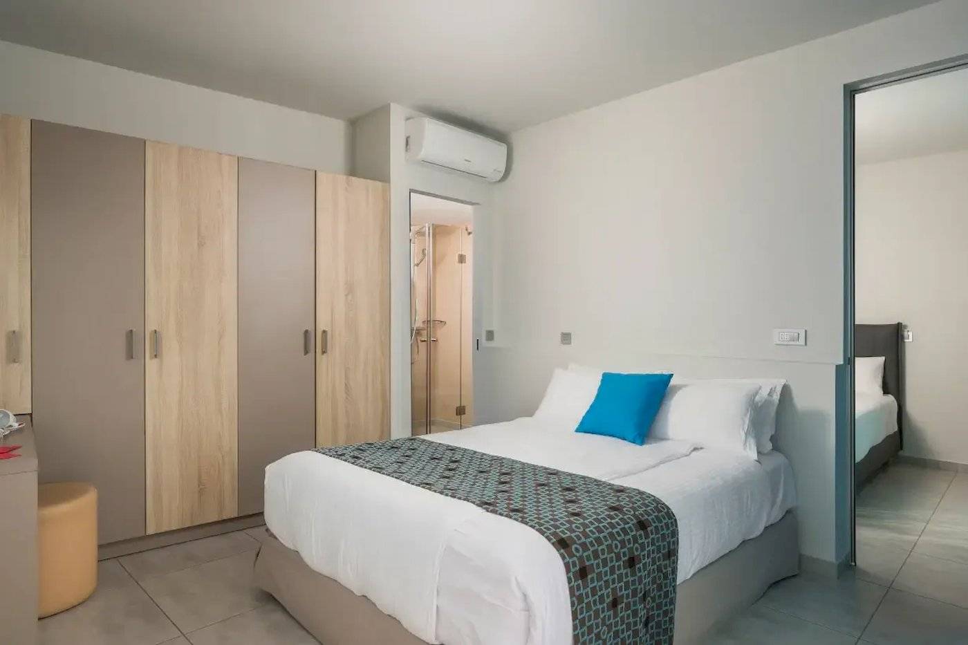 Innenansicht eines Zimmers im Corissia Beach Hotel mit einem Bett, Kissen, Decken und Holzschränken.