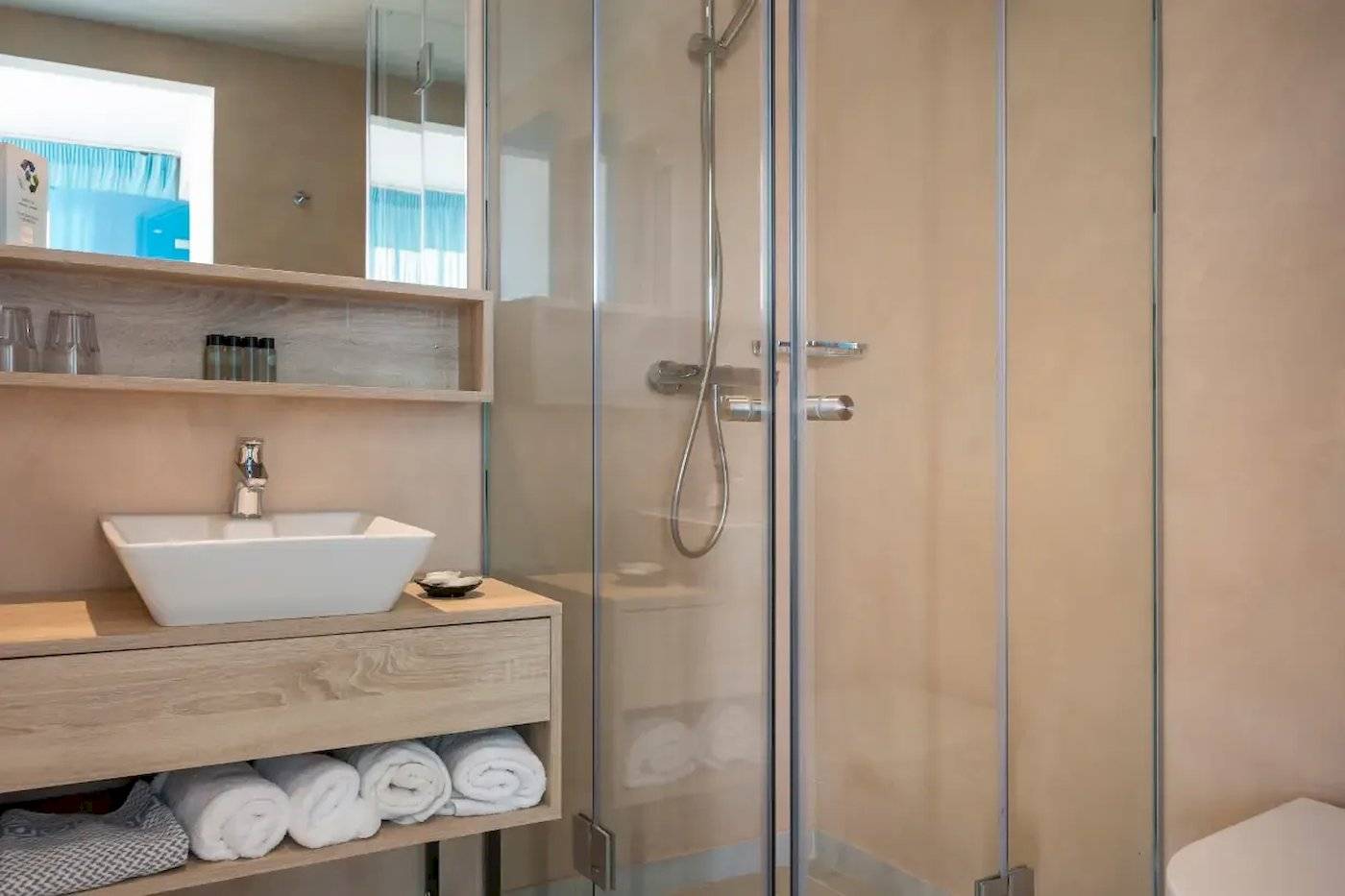 Badezimmer im Corissia Beach Hotel mit Glasdusche, Waschbecken und Handtüchern