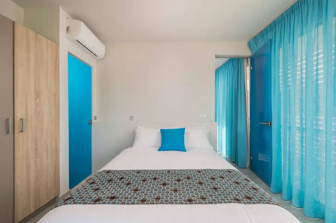 Schlafzimmer im Corissia Beach Hotel mit blauen Türen, einem Bett und einem blauen Kissen.