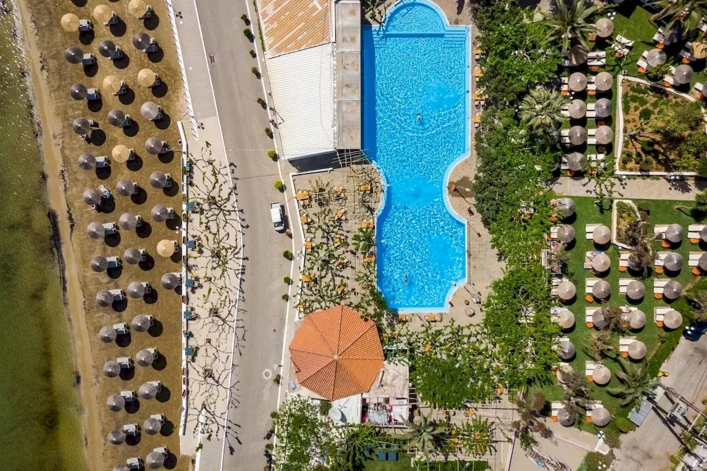 Luftaufnahme des Corissia Beach Hotels mit Swimmingpool, Sonnenschirmen und Liegen.