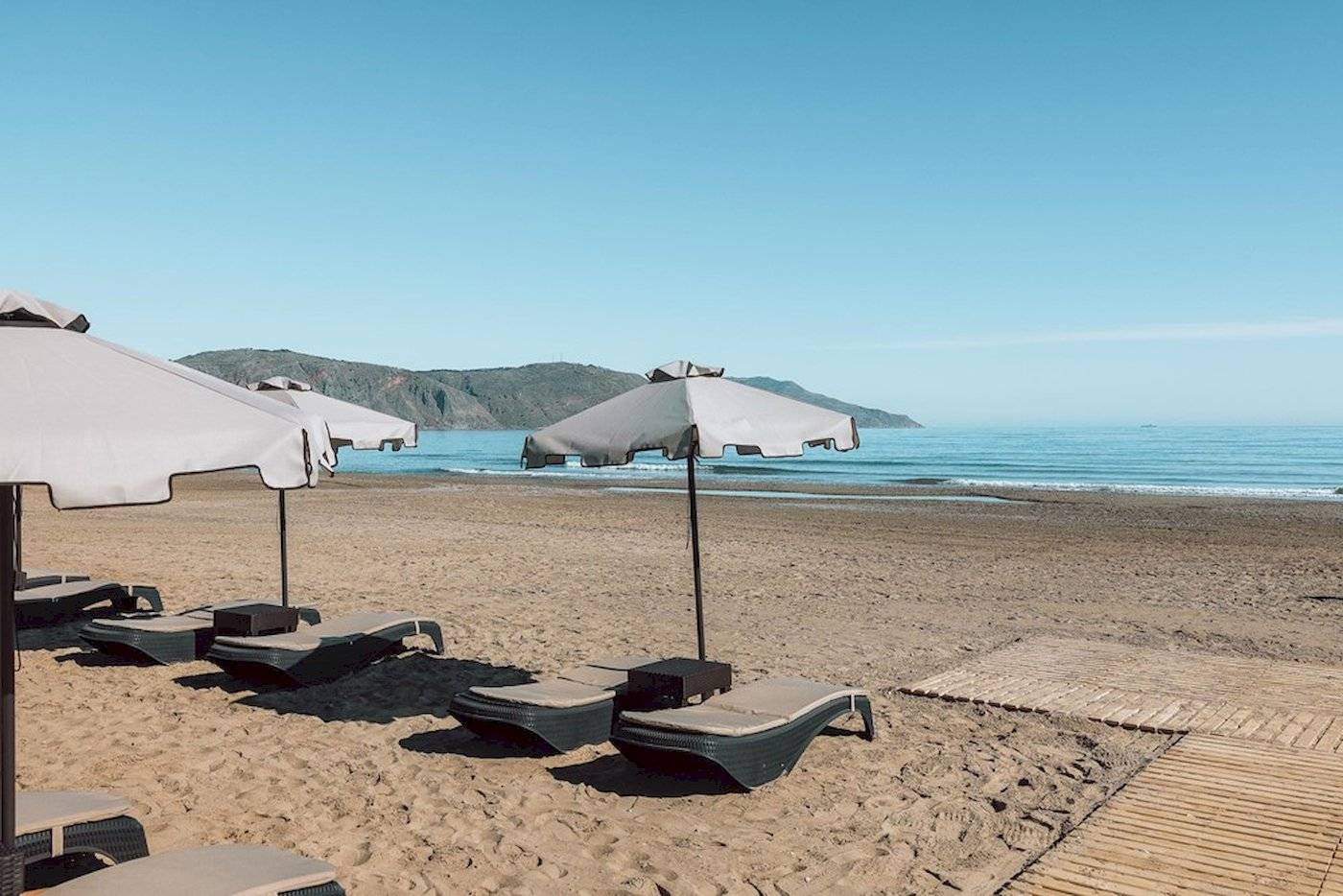 Eine Reihe von Sonnenliegen mit Sonnenschirmen auf dem Strand des Eliros Mare Hotels