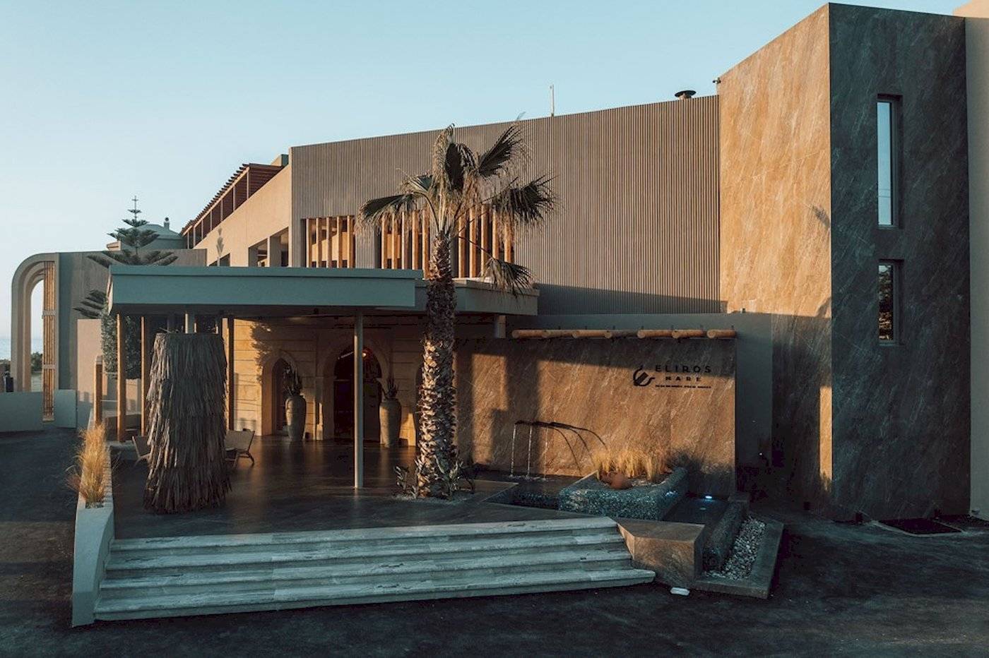 Außenansicht des Eliros Mare Hotels mit Eingang, Palme und Wasserbrunnen.