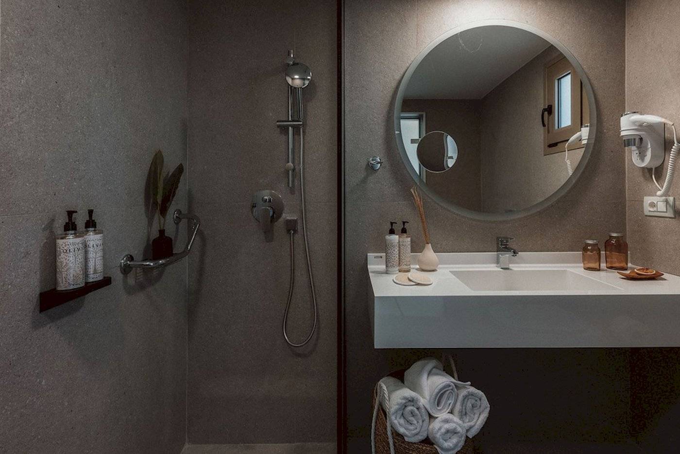 Badezimmer im Eliros Mare Hotel mit Dusche, Waschbecken und Handtüchern.