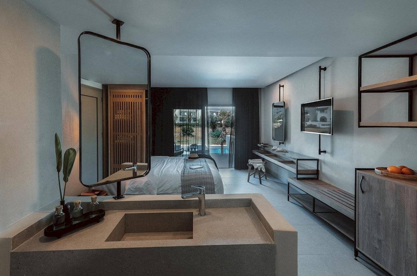 Innenansicht eines Zimmers im Eliros Mare Hotel mit Bett, Spiegel, Waschbecken und Pool im Hintergrund.