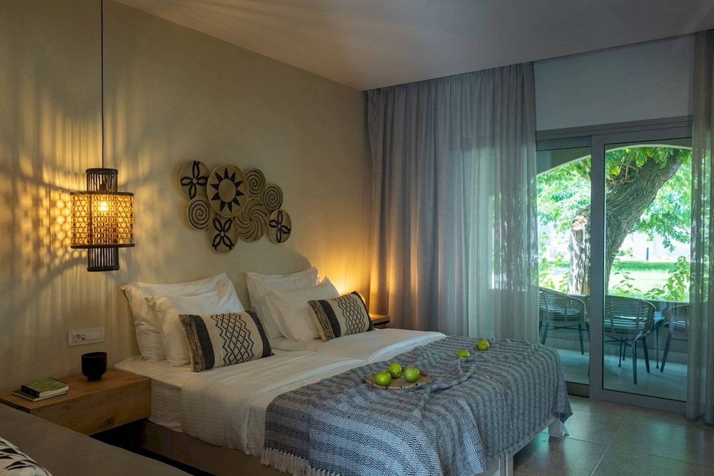 Schlafzimmer im Eliros Mare Hotel mit zwei Betten, Kissen, Bettwäsche, Lampen und offenem Balkon.