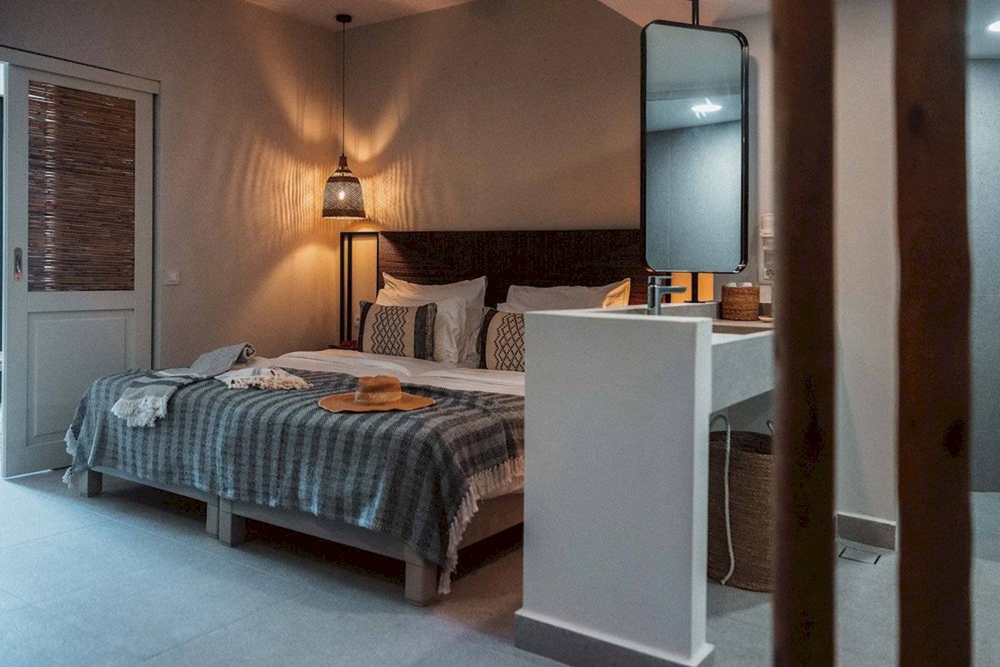 Schlafzimmer im Eliros Mare mit Bett, Decken, Kissen, Spiegel und Lampe.