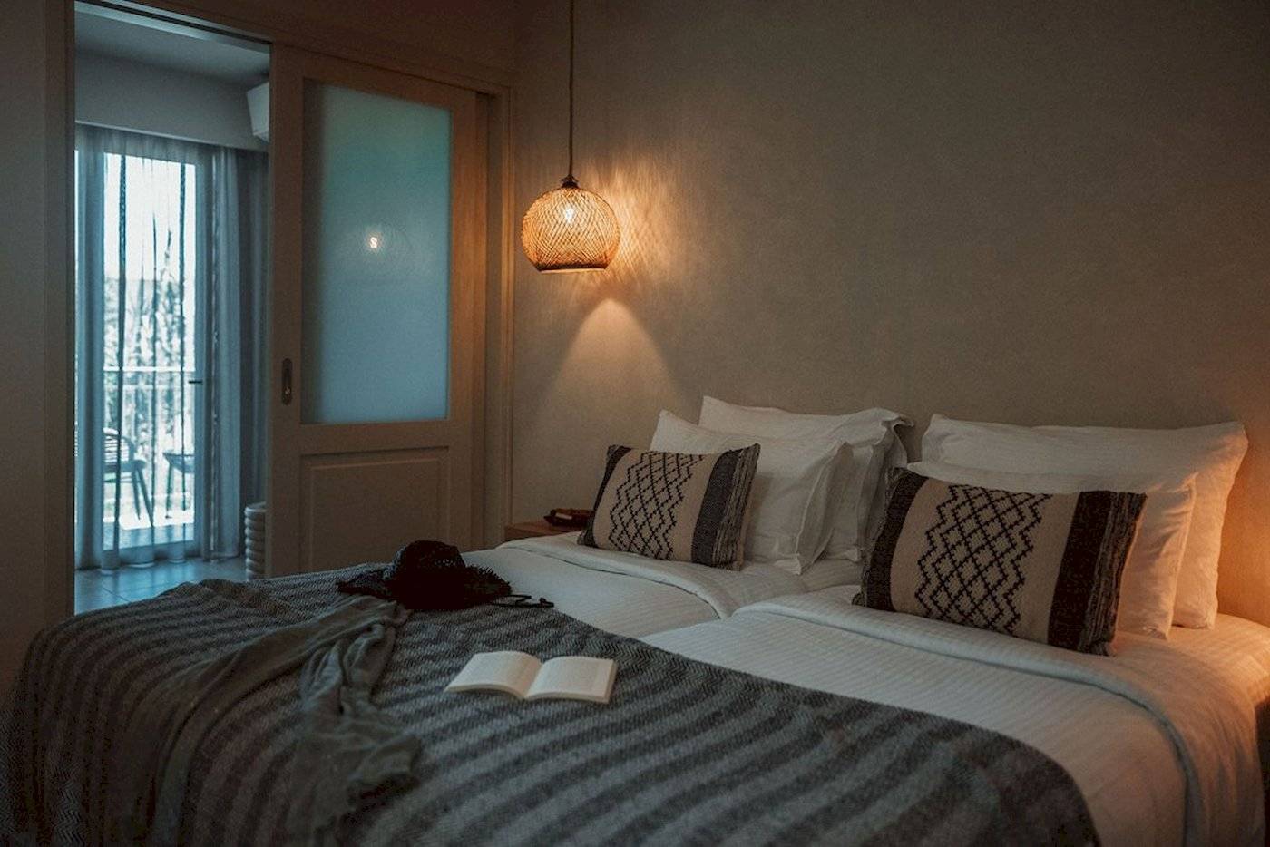 Doppelbettzimmer im Eliros Mare Hotel mit Bettwäsche, Kissen und einem offenen Buch auf der Bettdecke.