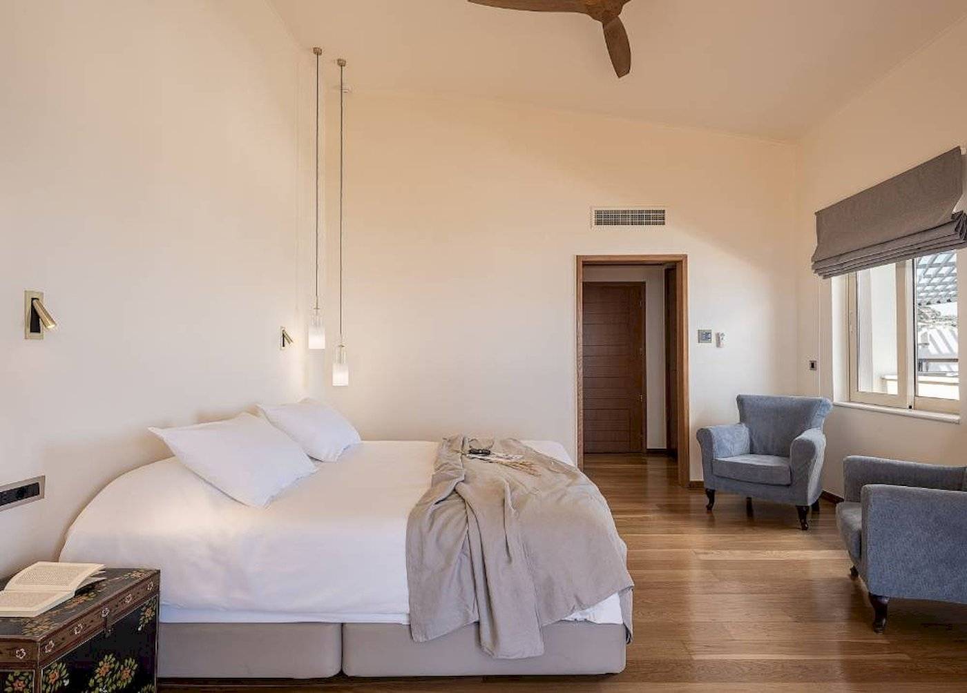 Schlafzimmer im Cretan Dream Resort & Spa mit großem Bett, Sesseln, Deckenventilator und Fenstern.