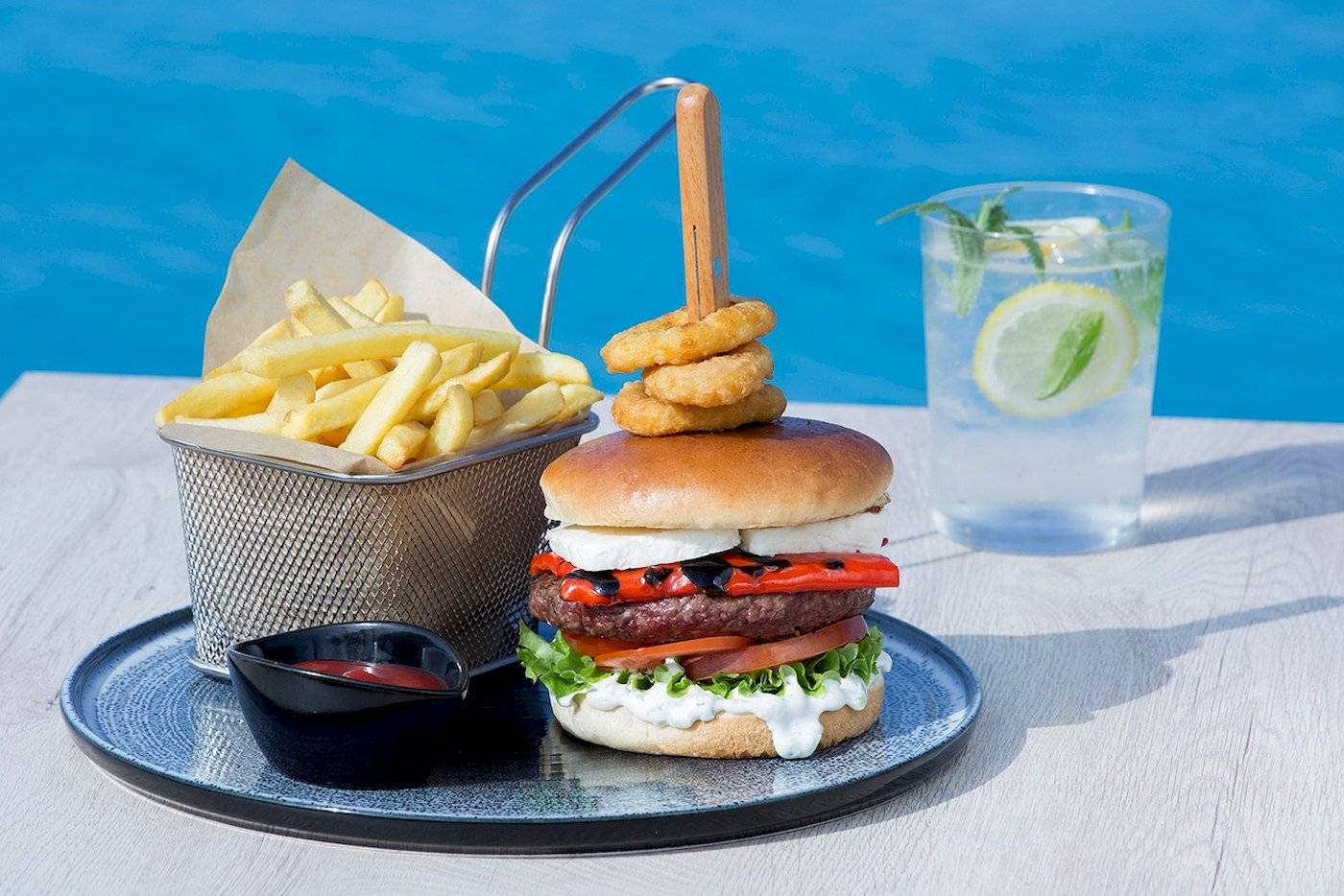 Ein Burger mit Pommes und Getränk am Pool des Cretan Dream Resort & Spa.