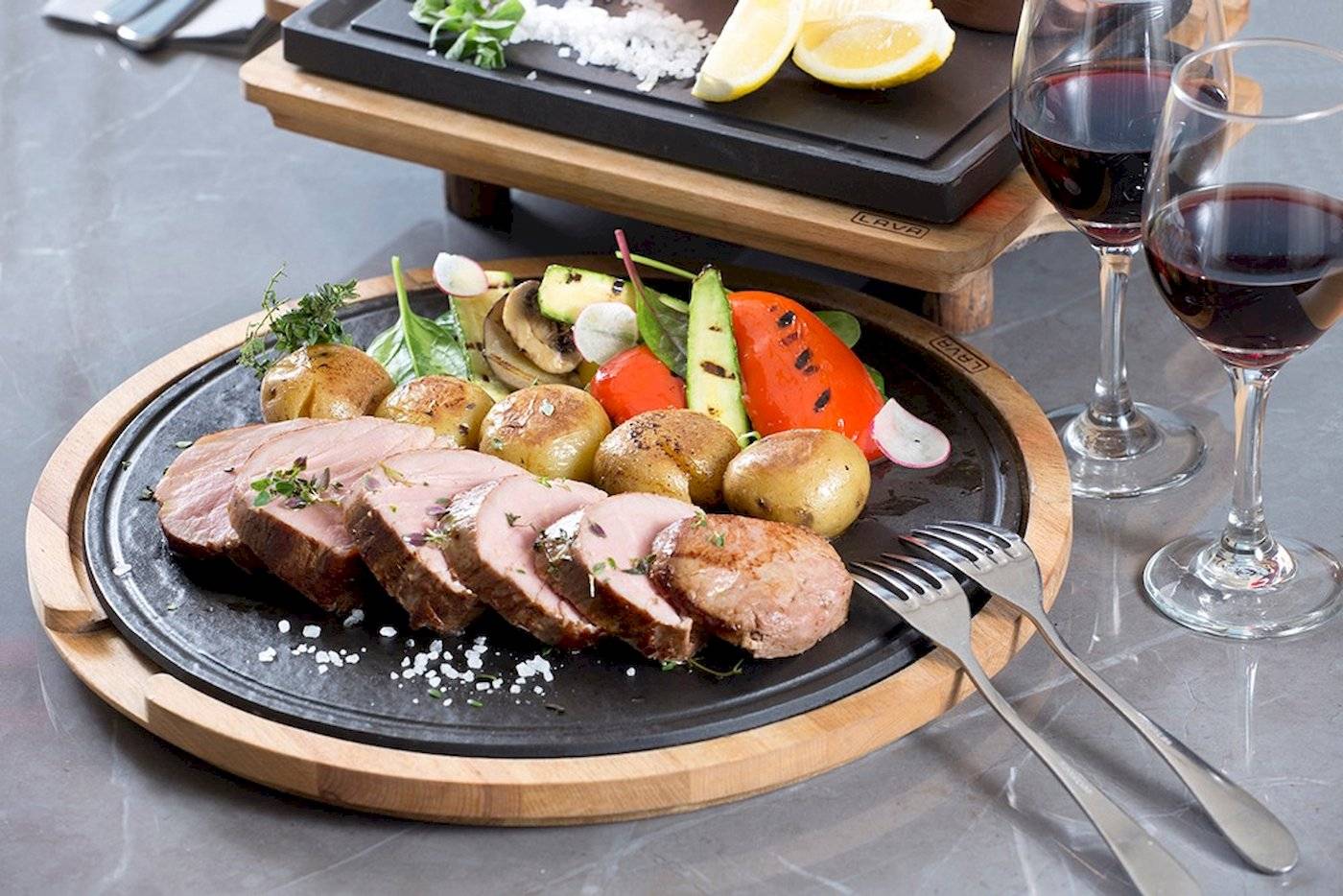 Fleischplatte mit Gemüse und zwei Weingläsern auf einem schwarzen Teller