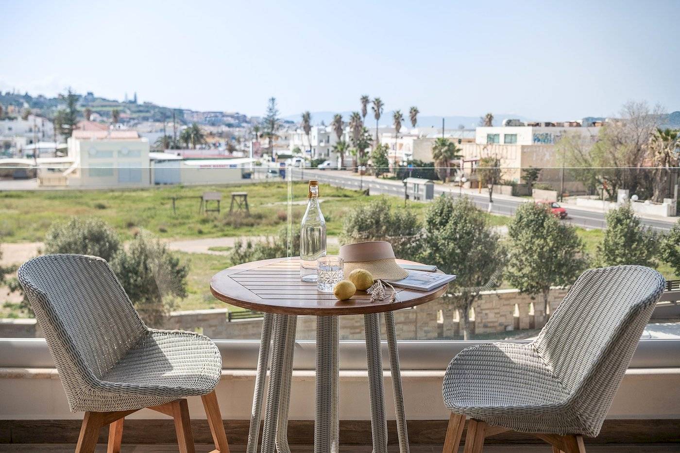 Zwei Stühle auf einem Balkon mit Aussicht auf eine Stadt, inklusive Tisch mit Flasche und Früchten.