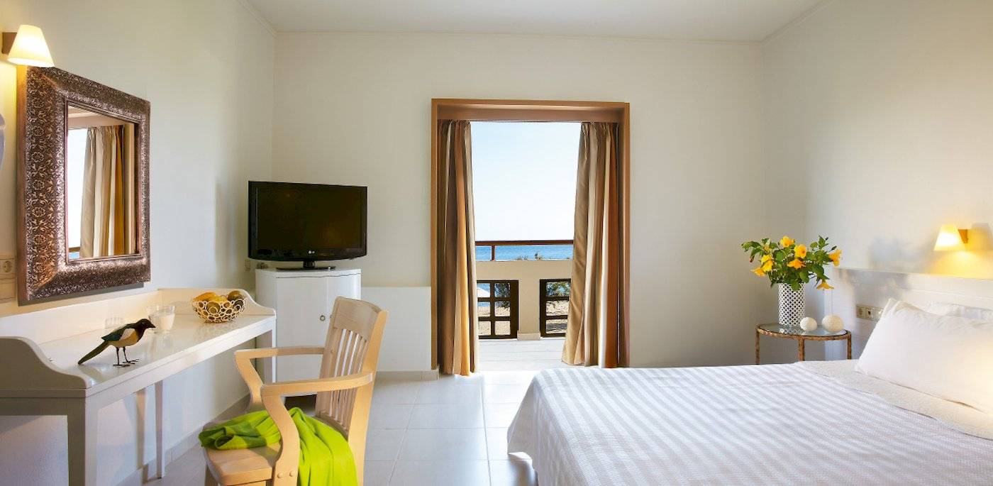 Innenansicht eines Hotelzimmers im Grecotel Meli Palace mit Bett, Schreibtisch und Balkon.