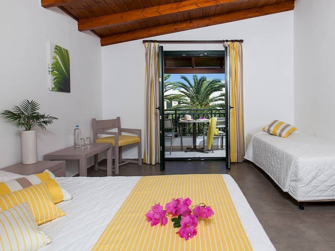Schlafzimmer im Chrissi Amoudia Hotel mit zwei Betten, Balkon und Palmenblick.