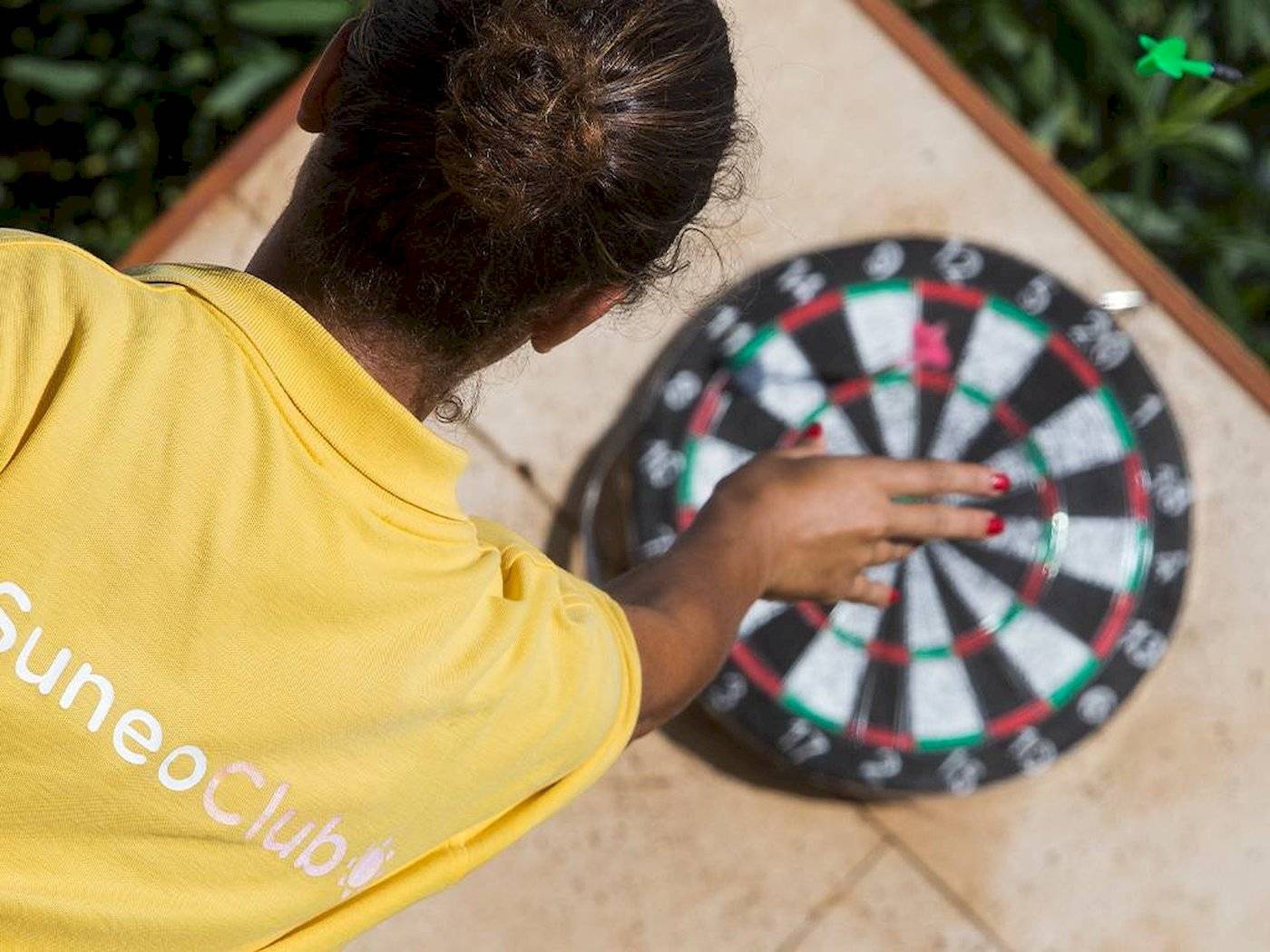 Eine Frau in einem gelben Suneo-Club-T-Shirt spielt Dart im Freien beim Chrissi-Amouida-Hotel.