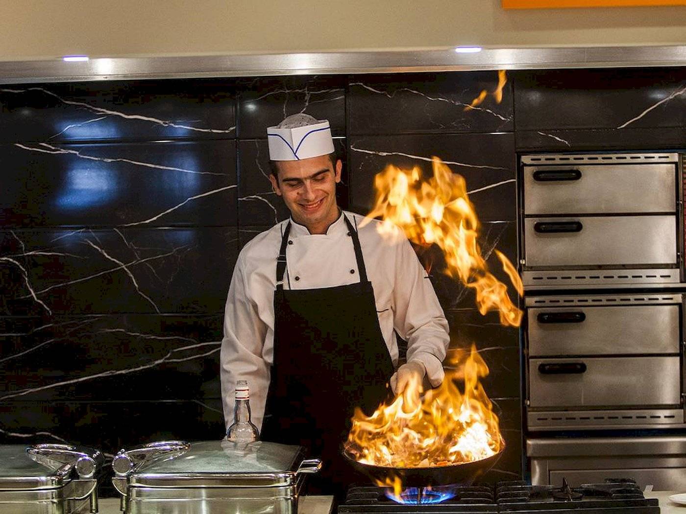 Koch im Chrissi Amoudia Hotel mit brennenden Flammen in der Küche