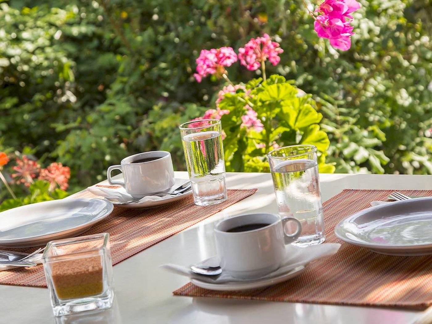 Frühstückstisch im Garten des Chrissi Amoudia Hotels mit Kaffee, Wasser und Gebäck.
