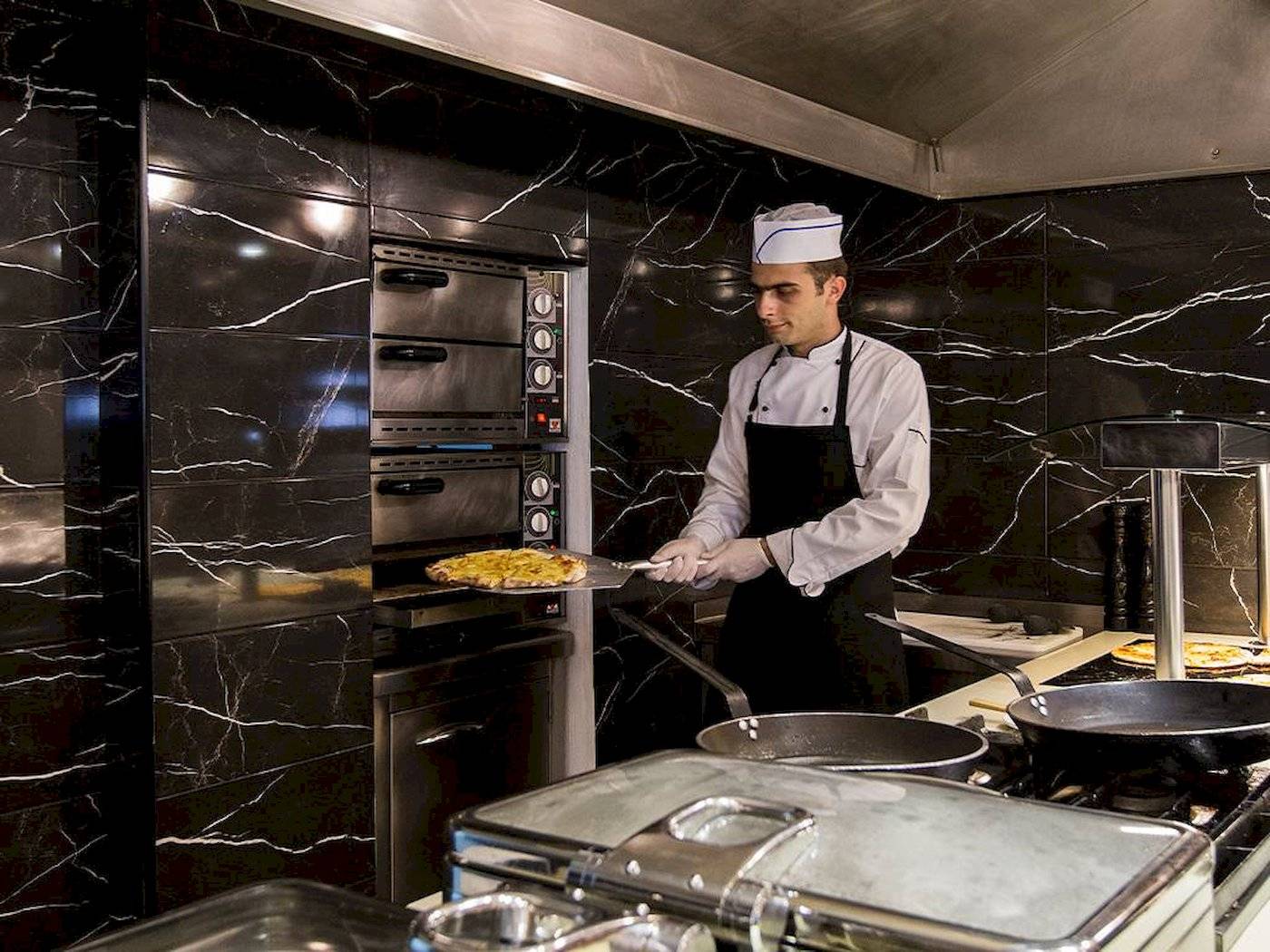 Koch im Chrissi Amoudia Hotel zieht Pizza aus dem Ofen