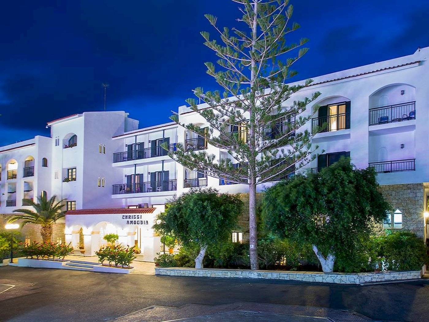 Die Außenansicht des Chrissi Amoudia Hotels bei Nacht mit einem großen Baum vor dem Gebäude.