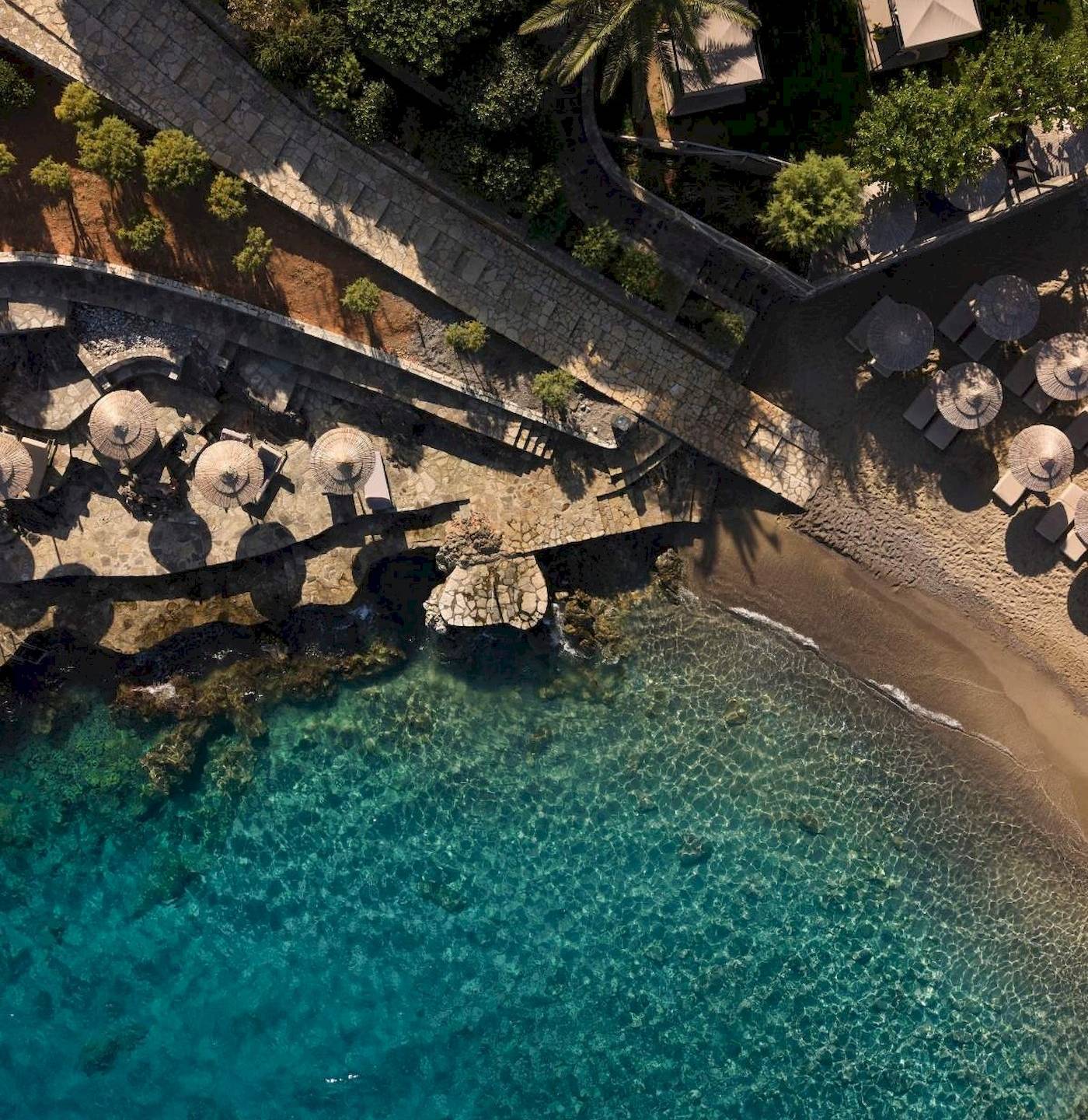 Luftaufnahme des Minos Palace Hotel & Suites am Strand mit Palmen und Sonnenschirmen.