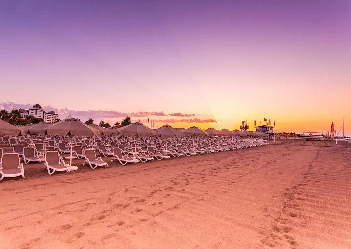 Strand mit Sonnenliegen und Sonnenschirmen vor dem Melas Lara Hotel bei Sonnenuntergang.